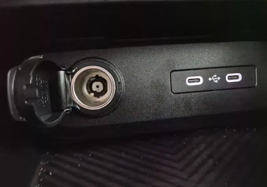 Prise allume-cigare ouverte et deux ports USB-C visibles sur la console centrale noire du Dacia Duster 2024.