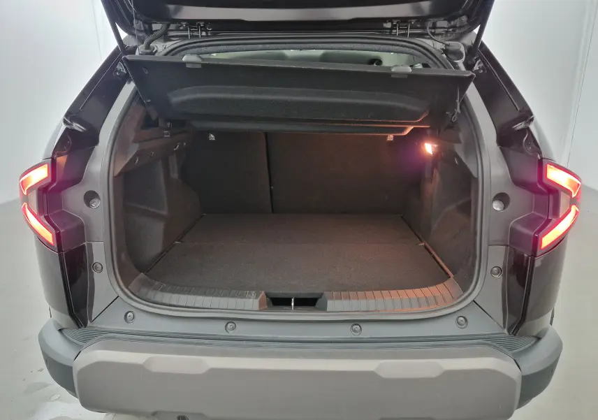 Coffre ouvert du Dacia Duster noir 2024 en vue arrière, avec feux arrière allumés et intérieur spacieux visible.