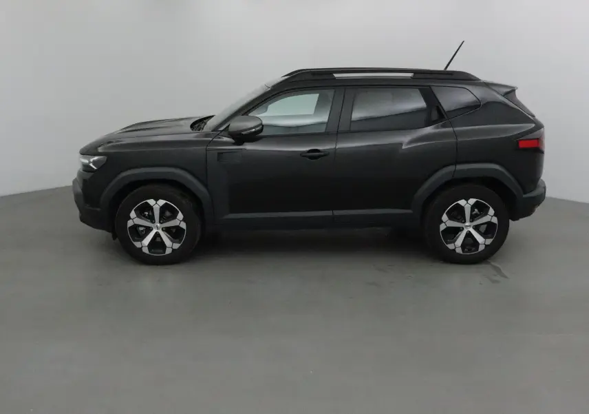 Profil côté gauche du SUV Dacia Duster 2024 noir, avec jantes alliage et barres de toit visibles.