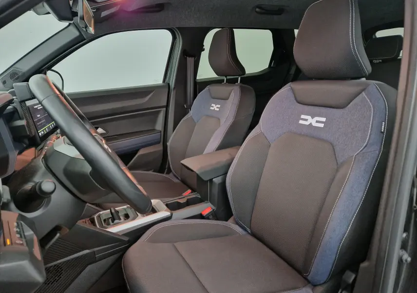 Vue intérieure côté conducteur du Dacia Duster 2024 avec sièges tissu bicolore et logo distinctif brodé.