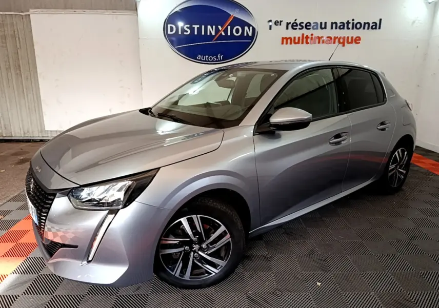 Peugeot 208 gris clair vue 3/4 avant droit dans un showroom avec jantes alliage et phares LED distinctifs.