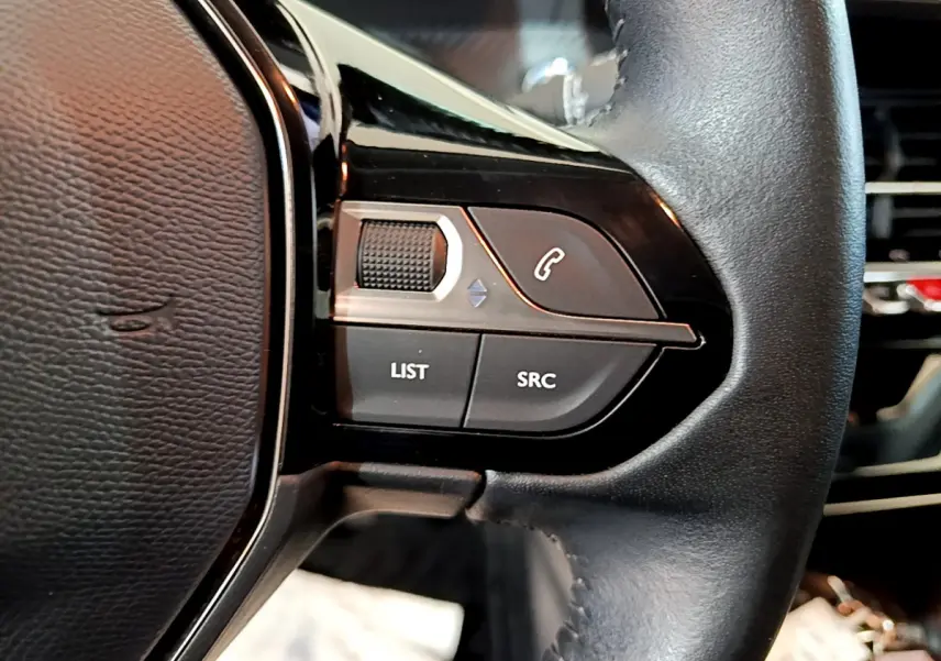 Gros plan sur les commandes gauche du volant cuir noir du Peugeot 208 gris clair, avec boutons LIST, SRC et téléphone.