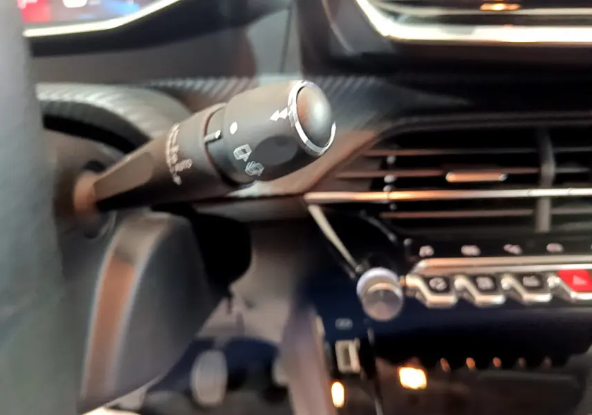 Gros plan sur la commande d’essuie-glace et la console centrale noire du tableau de bord d’une Peugeot 208 gris clair.