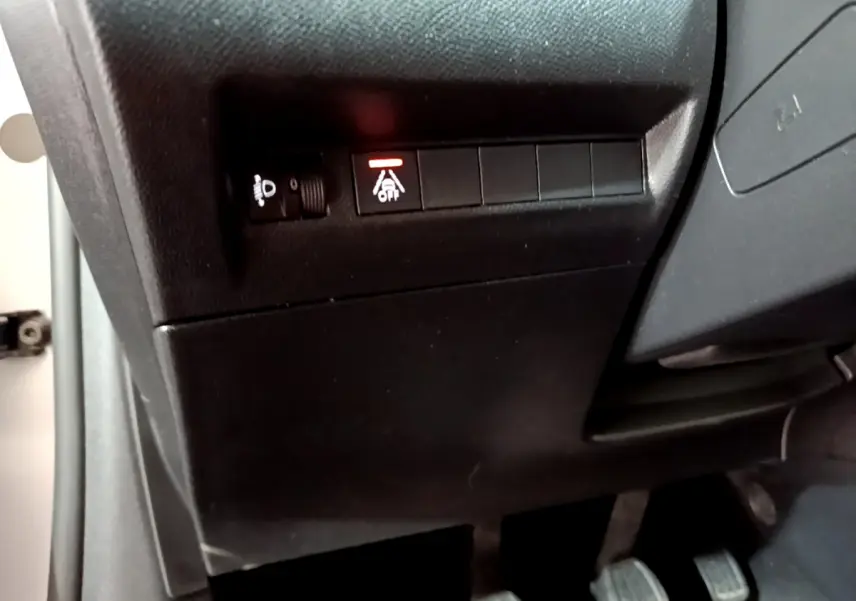 Vue rapprochée du tableau de bord côté gauche de la Peugeot 208 gris clair, montrant les commandes d'éclairage et d'aide à la conduite.