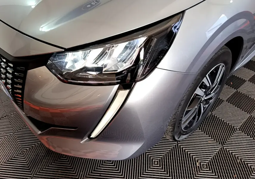 Gros plan sur l'avant droit gris clair d'une Peugeot 208 2020, mettant en valeur le phare LED et la jante alliage.
