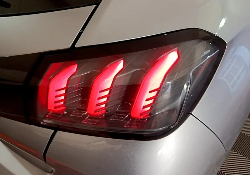 Gros plan sur le feu arrière droit allumé d'une Peugeot 208 gris clair, soulignant son design à trois griffes LED.