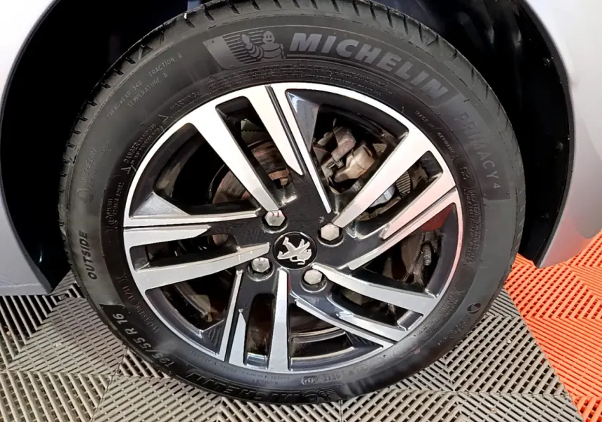 Gros plan sur la roue avant droite de la Peugeot 208 gris clair, jante alliage noire et argent avec logo lion central.