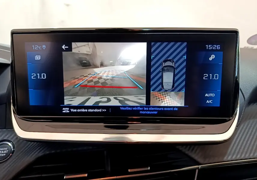 Écran tactile central affichant la caméra de recul et l'aide au stationnement dans une Peugeot 208 gris clair, vue intérieure.