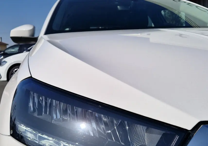 Gros plan sur le phare avant gauche d'une Skoda Fabia berline blanche 2022, avec calandre chromée visible.