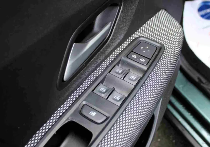 Gros plan sur la commande des vitres électriques côté conducteur du Dacia Jogger vert cèdre métal, avec poignée intérieure grise.