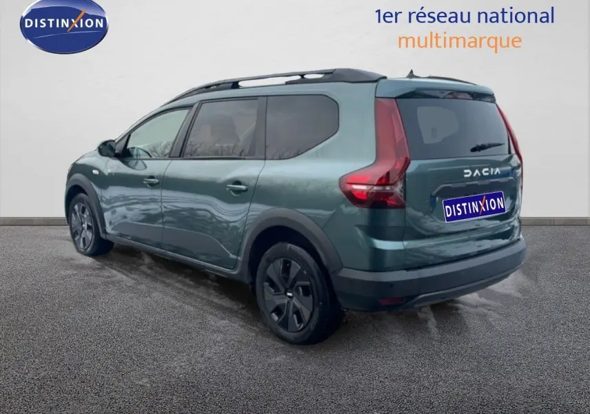 Vue 3/4 arrière gauche d'un Dacia Jogger 2025 vert cèdre métallisé avec toit noir et jantes foncées.