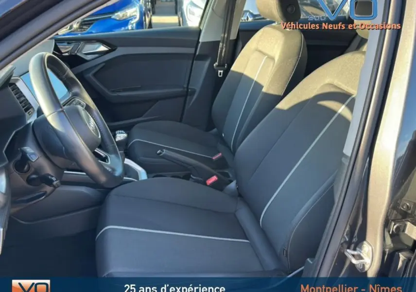 Vue intérieure côté conducteur de l'Audi A1 Sportback gris foncé, avec sièges tissu et volant cuir visible.