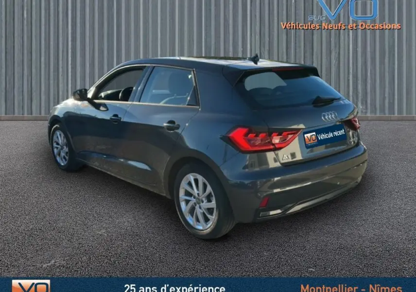Audi A1 Sportback gris foncé vue 3/4 arrière côté gauche, avec jantes 16 pouces et feux arrière allumés.