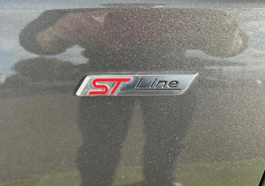 Gros plan sur le badge ST-Line rouge et noir sur la carrosserie gris metallic d'une Ford Focus IV.