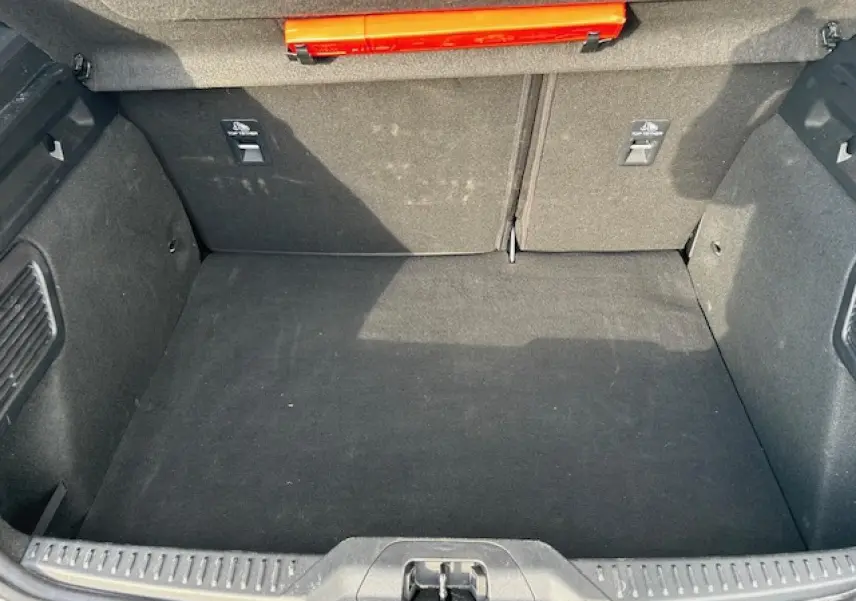 Vue plongeante sur le coffre spacieux et propre de la Ford Focus IV gris Magnetic Metal, avec tapis noir et rangement intégré.