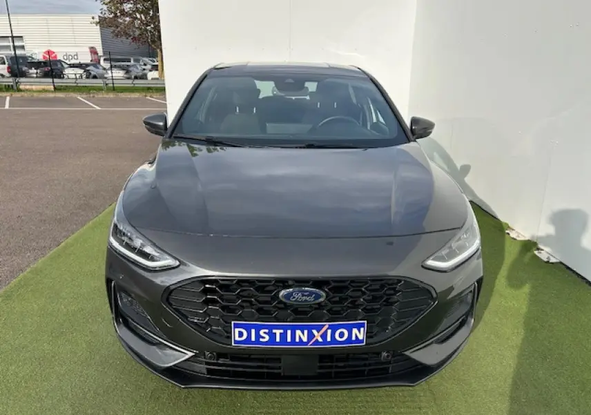 Ford Focus IV ST-Line X gris métallisé vue de face avec calandre noire et plaques Distinxion sur sol vert.