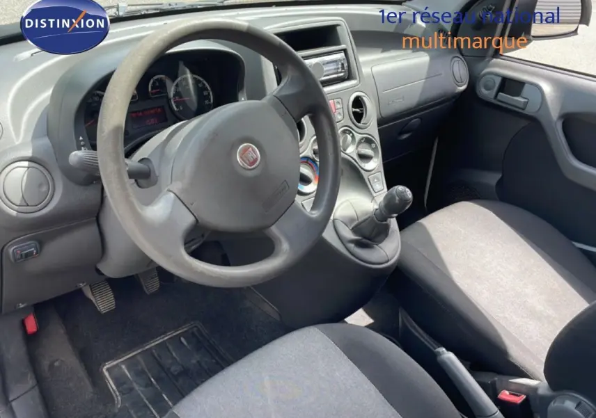 Vue intérieure côté conducteur de la Fiat Panda blanche 2011, volant, tableau de bord et sièges en tissu gris visibles.