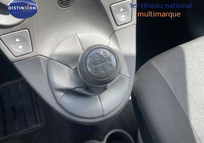 Gros plan sur le levier de vitesses manuel noir de la Fiat Panda blanche, avec siège tissu gris visible à droite.