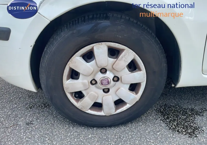 Gros plan sur la roue avant gauche blanche d'une Fiat Panda 2011 avec jante en plastique et logo Fiat au centre.