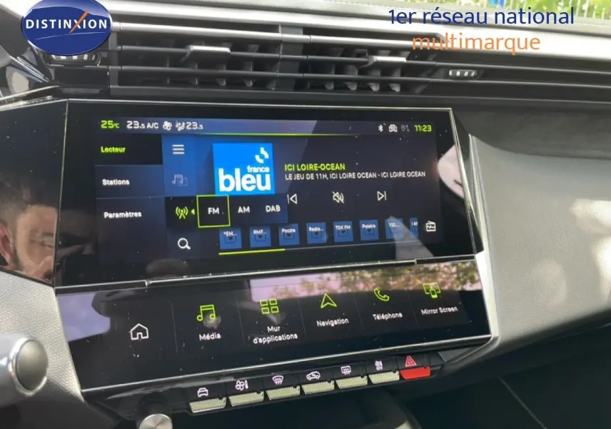 Vue rapprochée de l’écran tactile central du tableau de bord du Peugeot 308 gris Artense, affichant la radio FM.