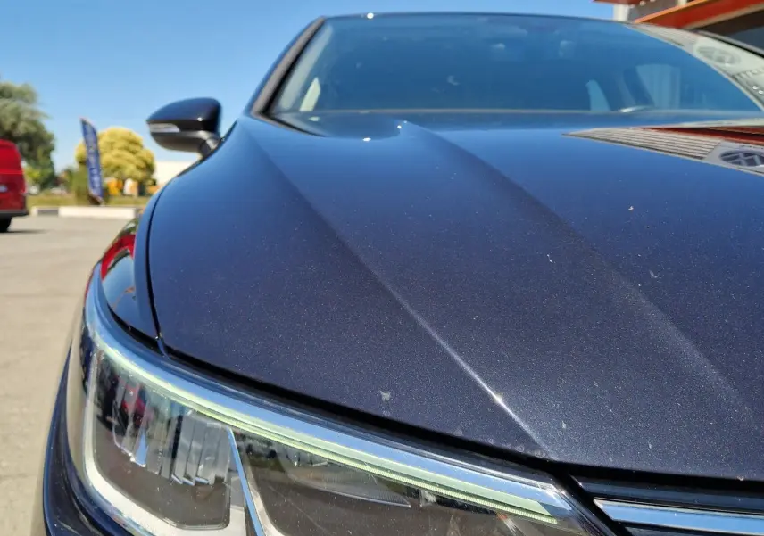 Gros plan sur le phare avant gauche d'une Volkswagen Golf VIII noire métal sous un ciel bleu clair.