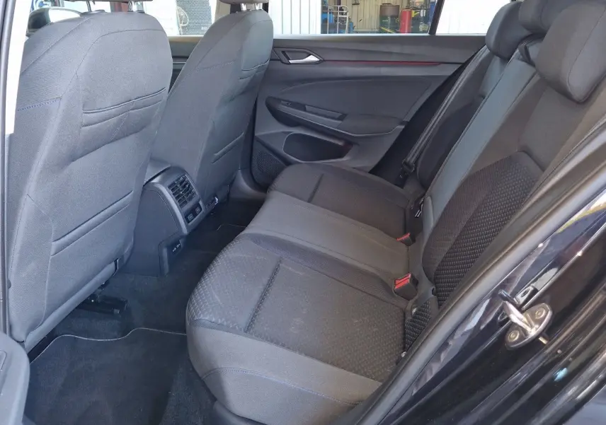 Intérieur arrière côté gauche d'une Volkswagen Golf VIII noire, sièges tissu gris et espace passagers visible.