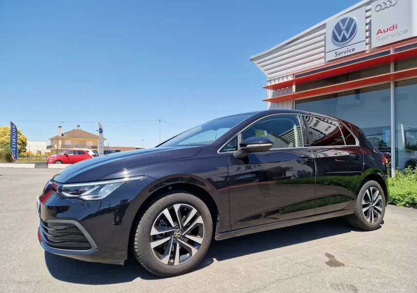 Volkswagen Golf VIII noire métal vue 3/4 avant droit, garée devant un service Audi sous un ciel bleu.