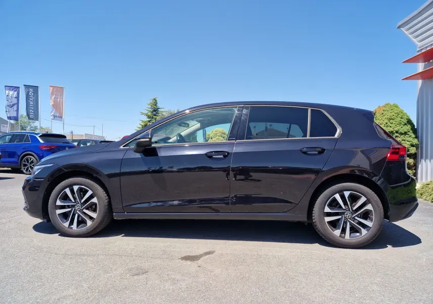 Profil droit d'une Volkswagen Golf VIII noire métallisée, mettant en valeur ses jantes alliage et sa silhouette compacte.
