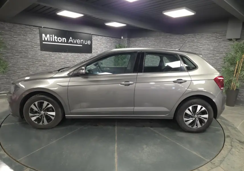 Profil côté gauche d'une Volkswagen Polo gris métallisé 2020 avec jantes alliage et vitres teintées en intérieur showroom.