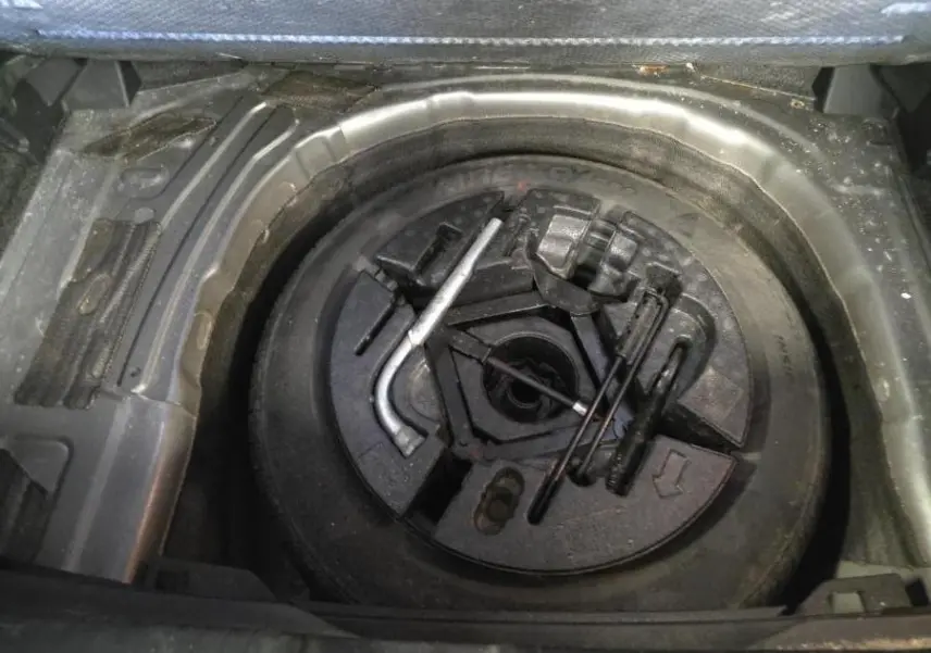 Vue en plongée sur la roue de secours et les outils de bord du coffre d'une Volkswagen Polo gris Urano 2020.