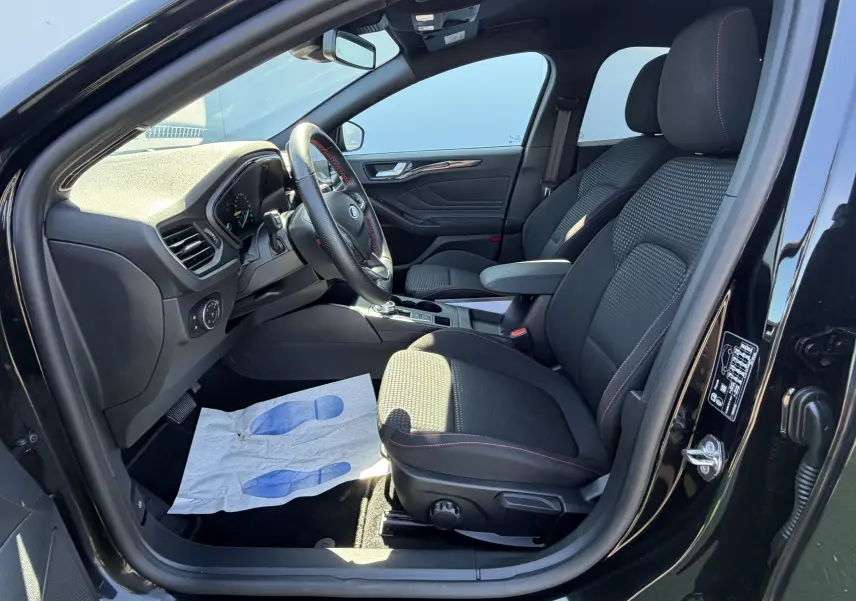 Vue intérieure côté conducteur de la Ford Focus IV ST-Line noire, sièges tissu avec surpiqûres rouges et volant sport.