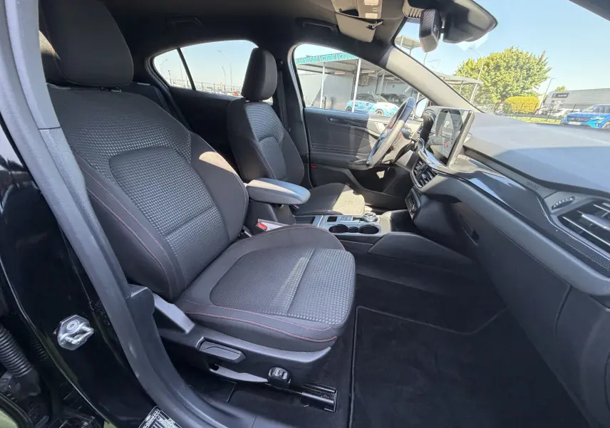 Intérieur avant droit de la Ford Focus IV noire, sièges tissu ST-Line avec surpiqûres rouges et tableau de bord moderne.