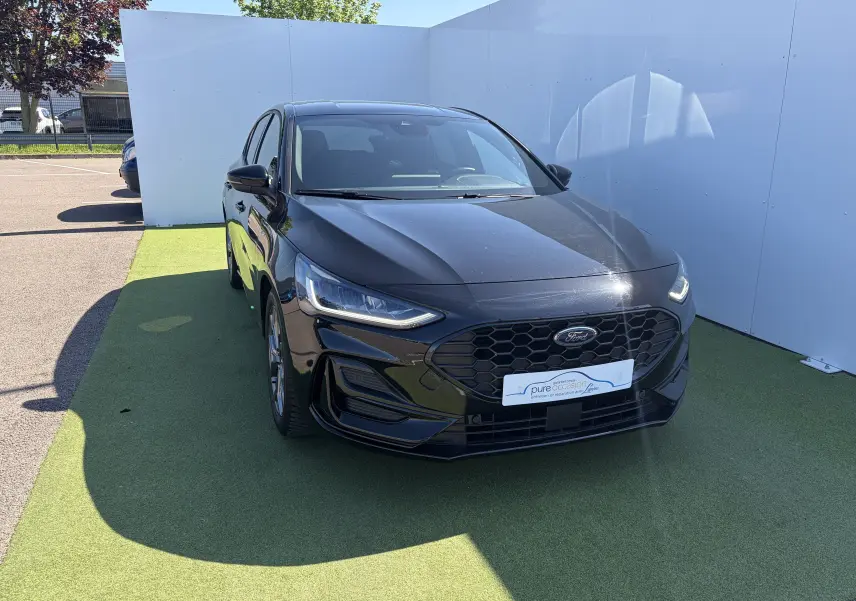 Ford Focus IV ST-Line X noire Agate vue 3/4 avant avec calandre noire et phares LED allumés.