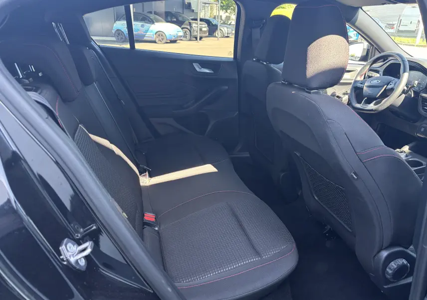 Vue intérieure arrière gauche de la Ford Focus IV ST-Line noire, sièges tissu avec surpiqûres rouges et banquette modulable.