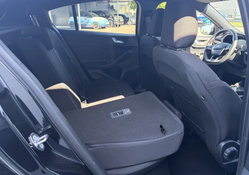 Vue intérieure côté gauche arrière de la Ford Focus IV noire, banquette rabattue avec surpiqûres rouges visibles sur les sièges.