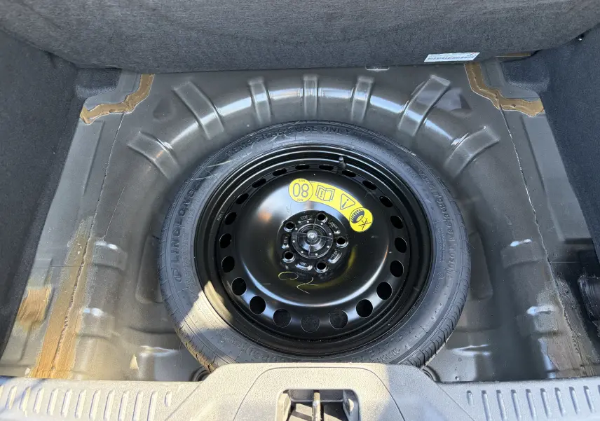 Vue plongeante sur la roue de secours noire dans le coffre d'une Ford Focus IV noire Agate, version ST-Line X.