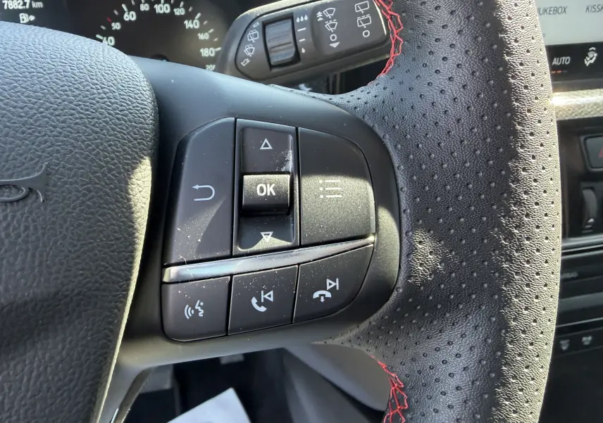 Gros plan sur la partie gauche du volant perforé noir avec surpiqûres rouges du Ford Focus IV ST-Line 2025, boutons multifonctions visibles.