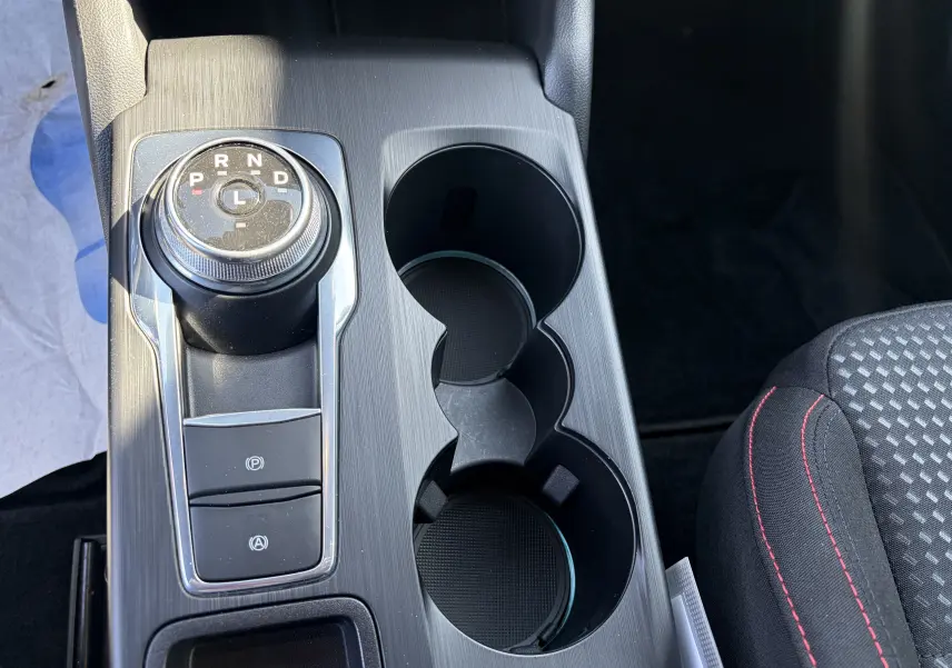 Vue rapprochée de la console centrale noire avec sélecteur rotatif de boîte auto et surpiqûres rouges sur siège tissu Ford Focus IV ST-Line.