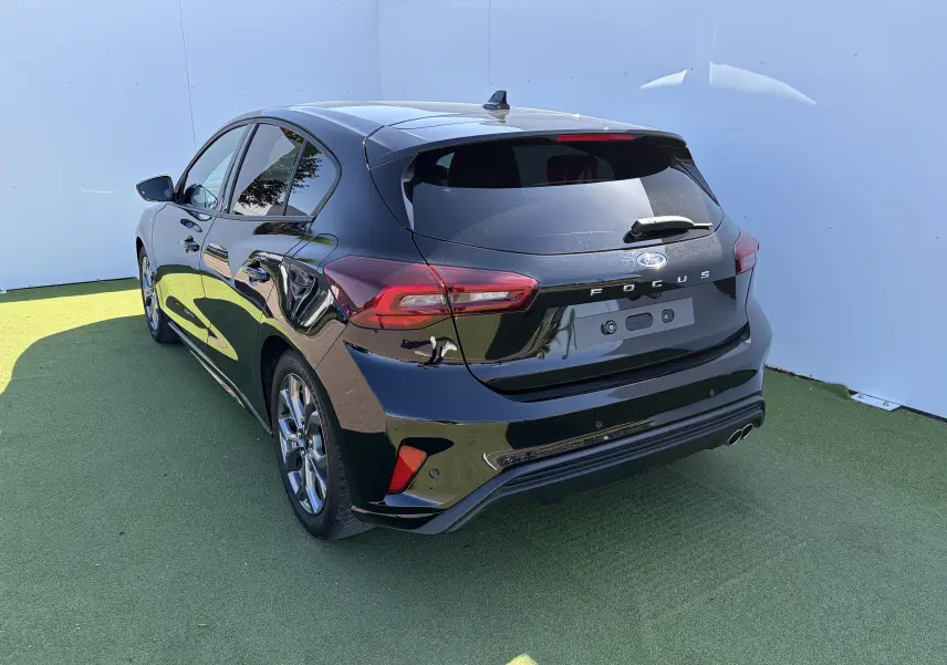 Ford Focus IV noire vue 3/4 arrière droit, avec double sortie d’échappement sport et jantes alliage 17 pouces.