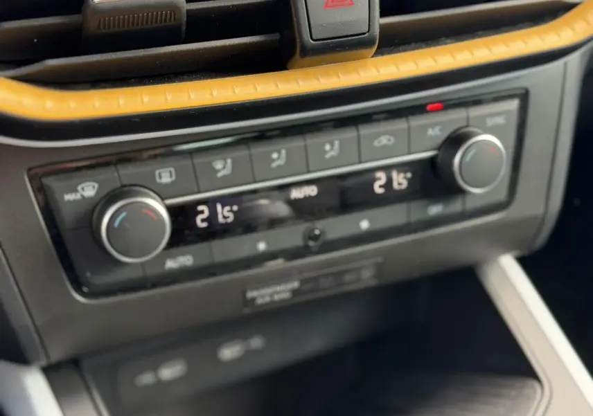 Gros plan sur la commande de climatisation automatique bi-zone du SEAT Arona, avec finition noire et insert jaune.