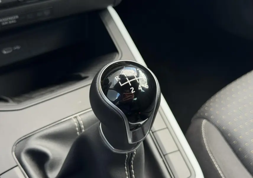 Gros plan sur le levier de vitesse manuel noir avec coutures blanches, intérieur tissu gris du SEAT Arona 2025.