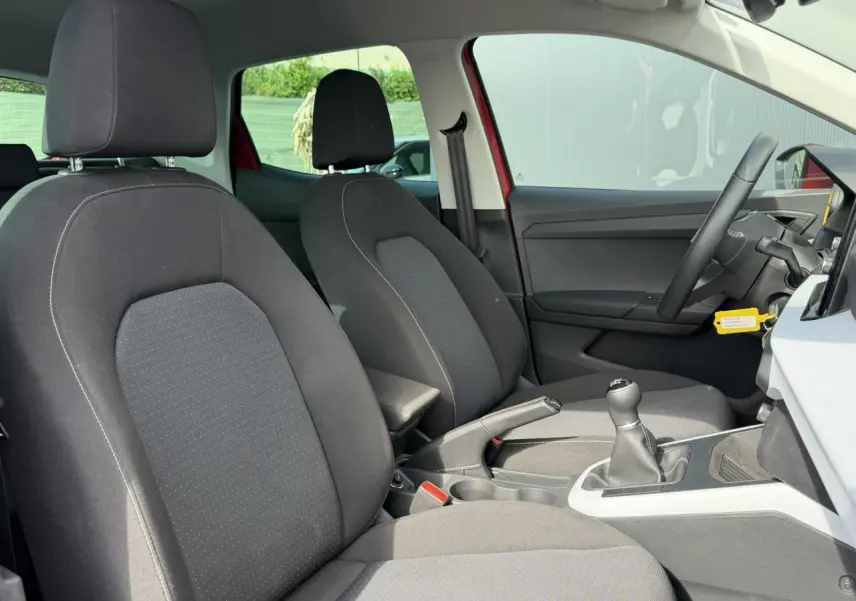 Intérieur avant du SEAT Arona rouge Désir 2025, vue côté droit montrant les sièges noirs et la boîte manuelle.
