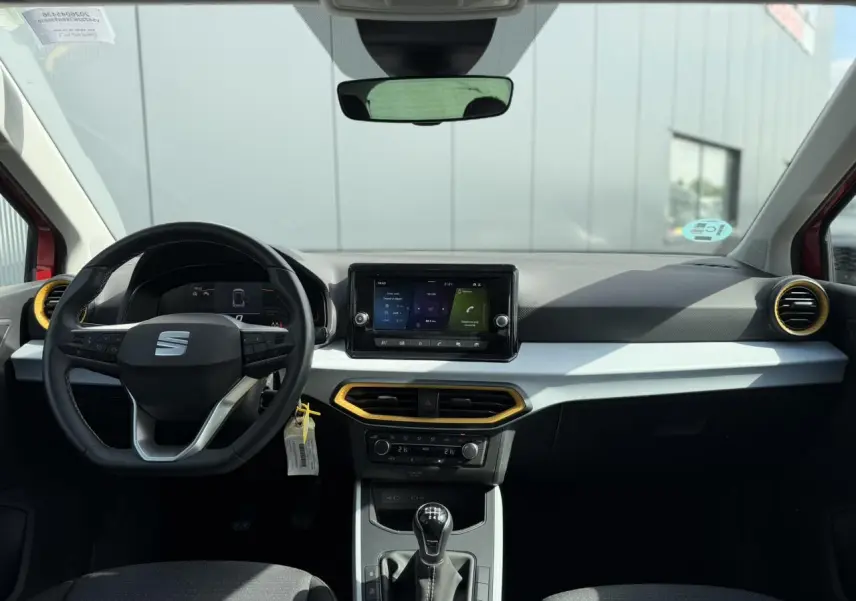 Vue intérieure frontale du poste de conduite du SEAT Arona rouge, avec volant multifonction, écran tactile et détails jaunes autour des aérateurs.