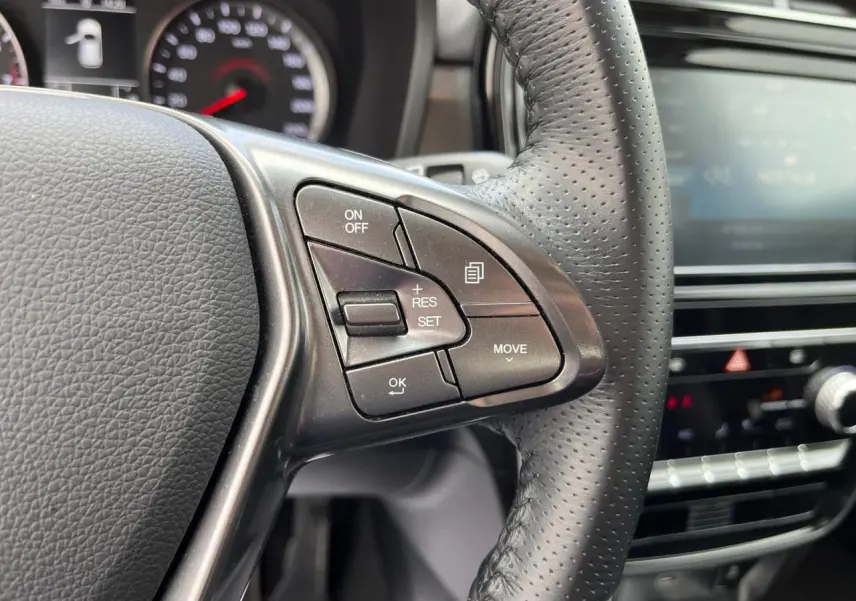 Gros plan sur le volant cuir perforé du SSANGYONG TIVOLI blanc 2021, avec commandes de régulateur de vitesse visibles.