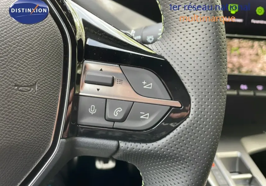 Gros plan sur les commandes gauche du volant perforé d'une Peugeot 308 gris Artense Hybrid 2026, avec boutons multifonctions.