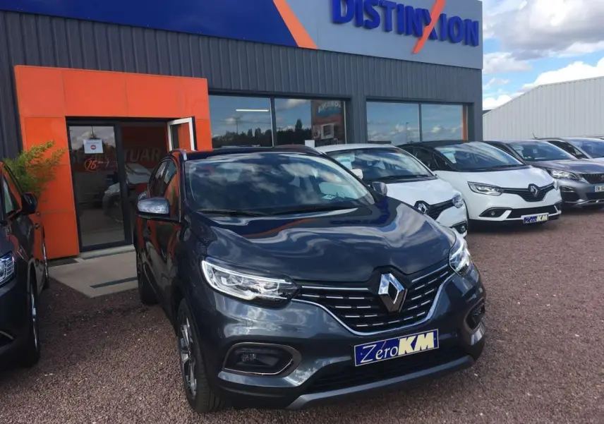 Vue 3/4 avant d'un Renault Kadjar gris titanium avec phares LED et jantes alliage 19 pouces devant un concessionnaire.