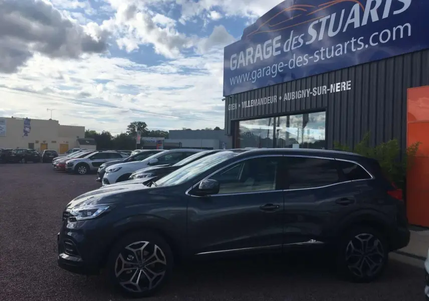Vue de profil côté gauche d’un Renault Kadjar 1.5 BlueDCi gris titanium avec jantes alliage diamantées, stationné devant un garage.
