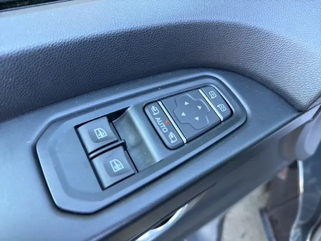 Gros plan sur les commandes électriques des vitres et des rétroviseurs sur la porte côté conducteur du Nissan Primastar gris foncé.