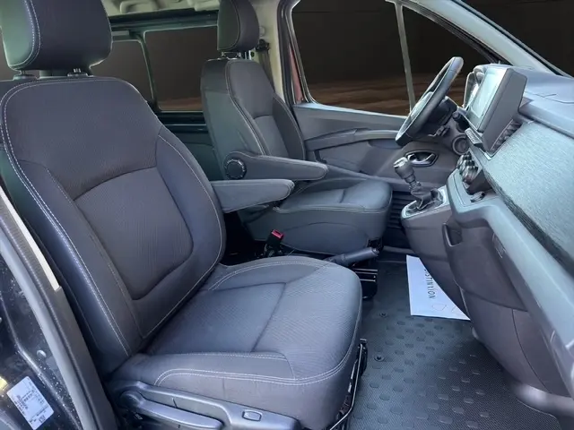 Intérieur avant du Nissan Primastar gris foncé, vue côté conducteur, sièges tissu et tableau de bord avec écran tactile.