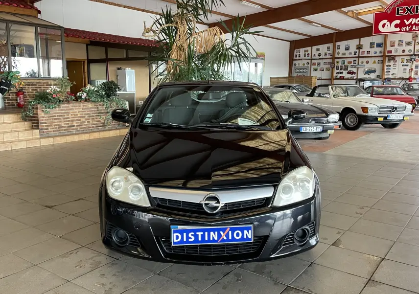 Opel Tigra Twintop noir vue de face en intérieur, avec plaque Distinxion et phares arrondis visibles.